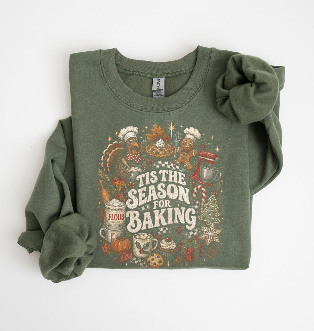 An olive green long-sleeve crewneck sweatshirt with a festive holiday baking graphic on the front, styled flat on a white background with one sleeve rolled up.
