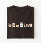A dark brown folded t-shirt on a white background, featuring a graphic print of baking ingredients including a bowl, flour, butter, sugar, vanilla, and eggs.