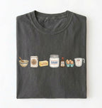A dark gray folded t-shirt on a white background, featuring a graphic print of baking ingredients including a bowl, flour bag, butter, sugar jar, vanilla bottle, eggs, and a measuring cup.