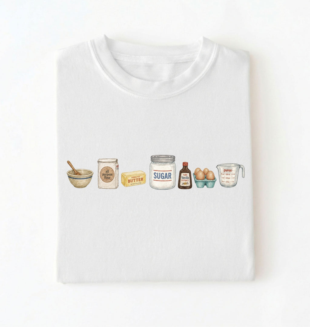 A white crewneck t-shirt with a watercolor-style graphic of baking ingredients (bowl, flour jar, butter, sugar jar, vanilla bottle, eggs, and measuring cup) across the chest, displayed flat against a white background.