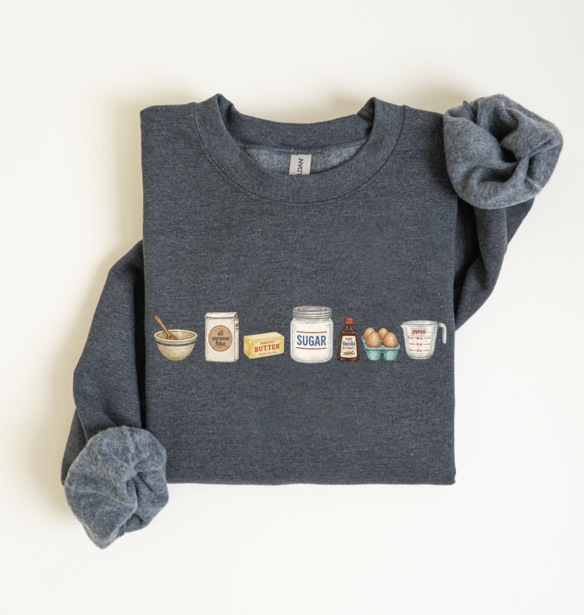 A dark heather gray crewneck sweatshirt with rolled-up sleeves, featuring a graphic print of baking ingredients (bowl, flour sack, butter, sugar jar, eggs, and measuring cup) across the chest, laid flat on a white background.