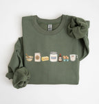 An olive green crewneck sweatshirt with rolled-up sleeves, featuring a graphic print of baking ingredients (flour, baking powder, butter, sugar, vanilla extract, eggs, and flour) on the chest, laid flat on a white background.