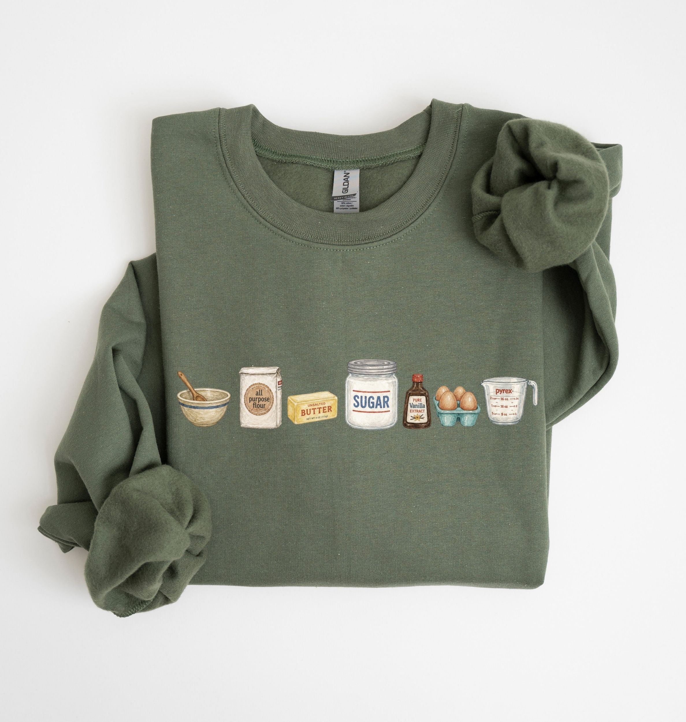 An olive green crewneck sweatshirt with rolled-up sleeves, featuring a graphic print of baking ingredients (flour, baking powder, butter, sugar, vanilla extract, eggs, and flour) on the chest, laid flat on a white background.