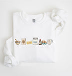A white crewneck sweatshirt featuring a graphic print of various baking ingredients (bowl, flour, butter, sugar, vanilla, eggs, measuring cup) arranged in a row, displayed on a clean white background.