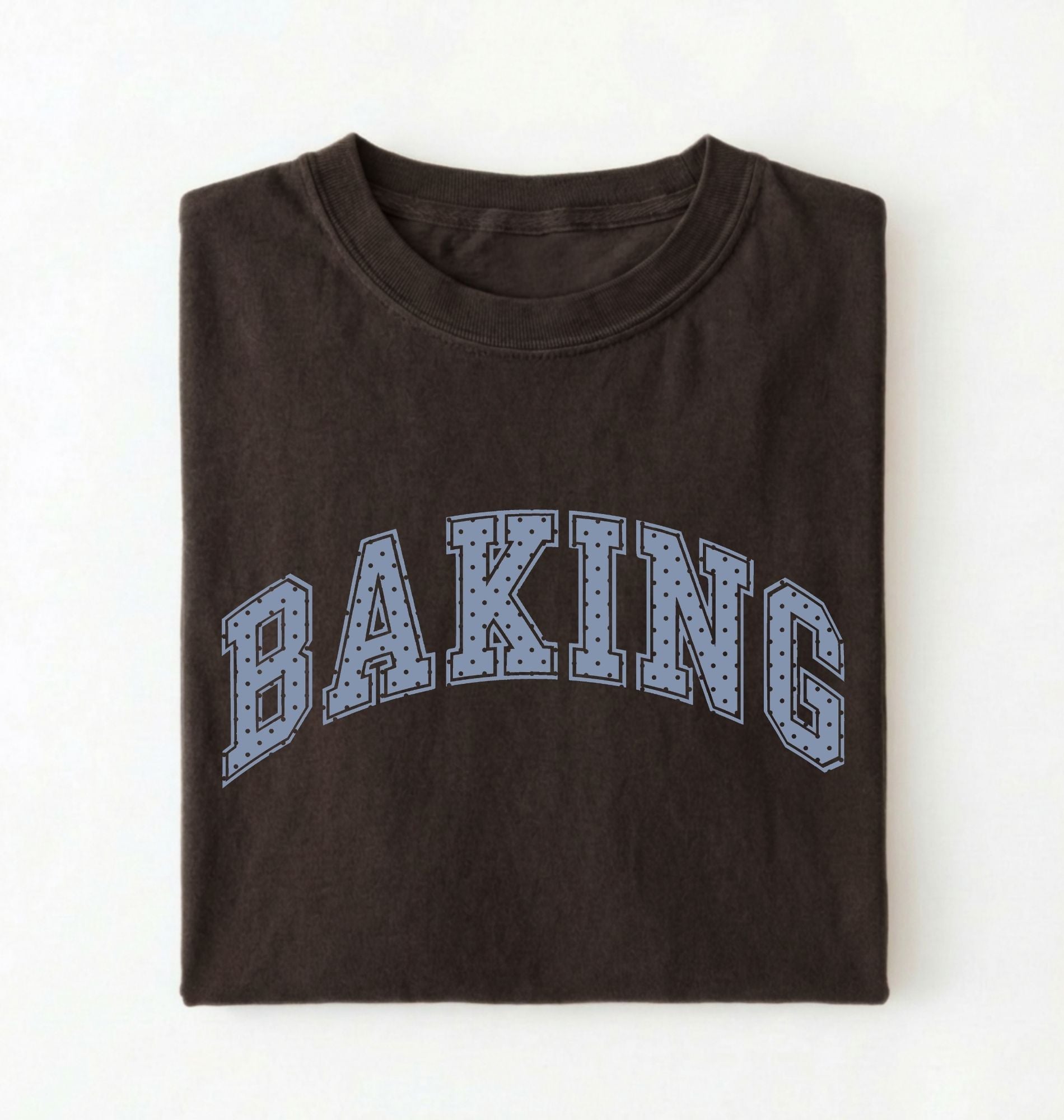 A folded dark brown t-shirt with the word 'BAKING' printed across the chest in arched varsity-style letters filled with a light blue dotted pattern, set against a plain white background.