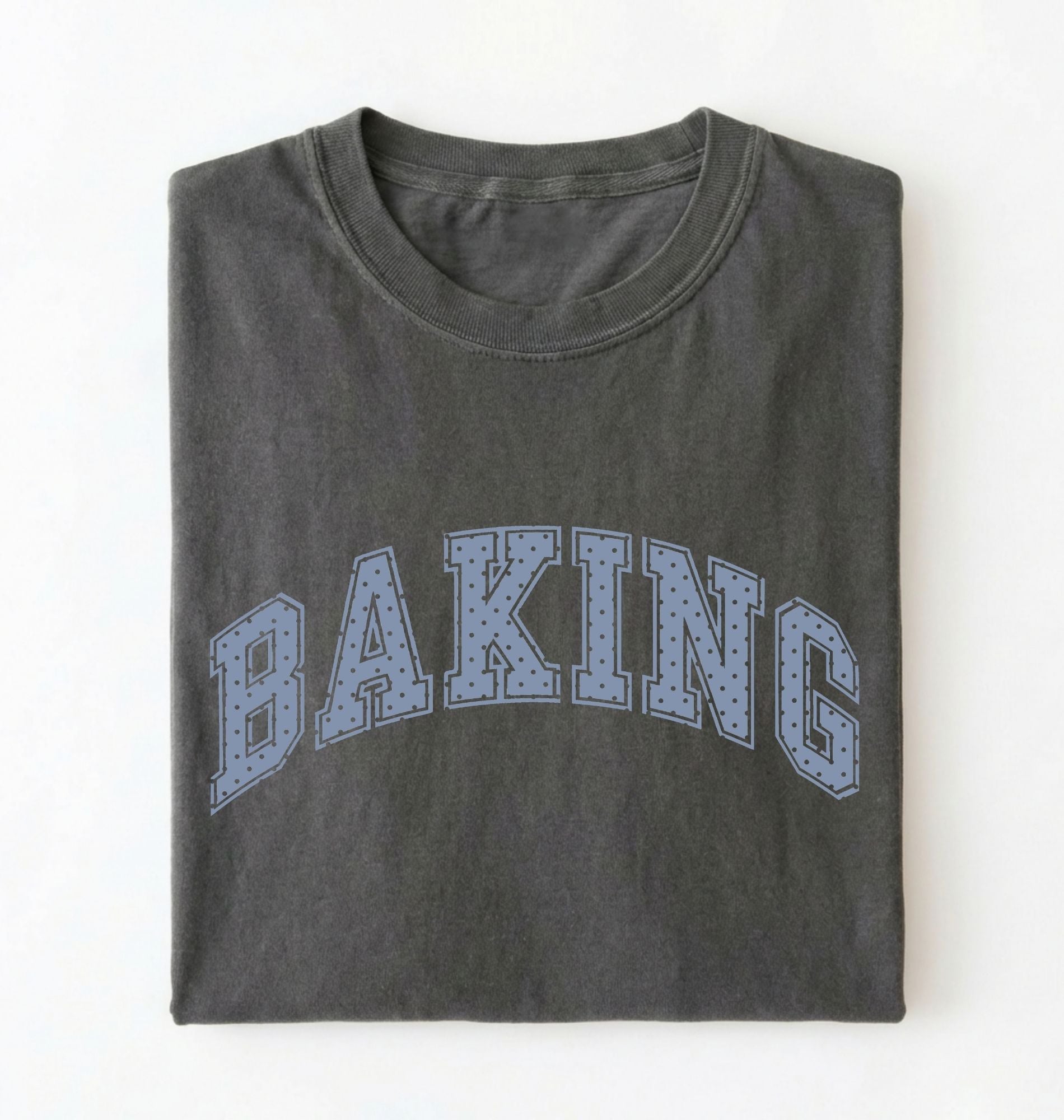 A dark gray folded t-shirt with the word 'BAKING' printed across the front in a light blue dotted collegiate-style font, shown against a plain white background.