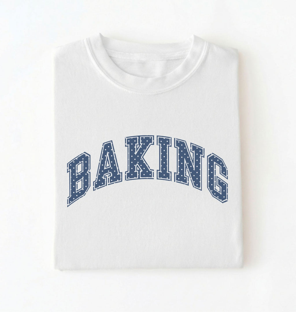 A folded white crewneck t-shirt with the word 'BAKING' printed in an arched navy blue varsity-style font with white dots, set against a plain white background.