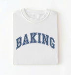 A folded white crewneck t-shirt with the word 'BAKING' printed in an arched navy blue varsity-style font with white dots, set against a plain white background.