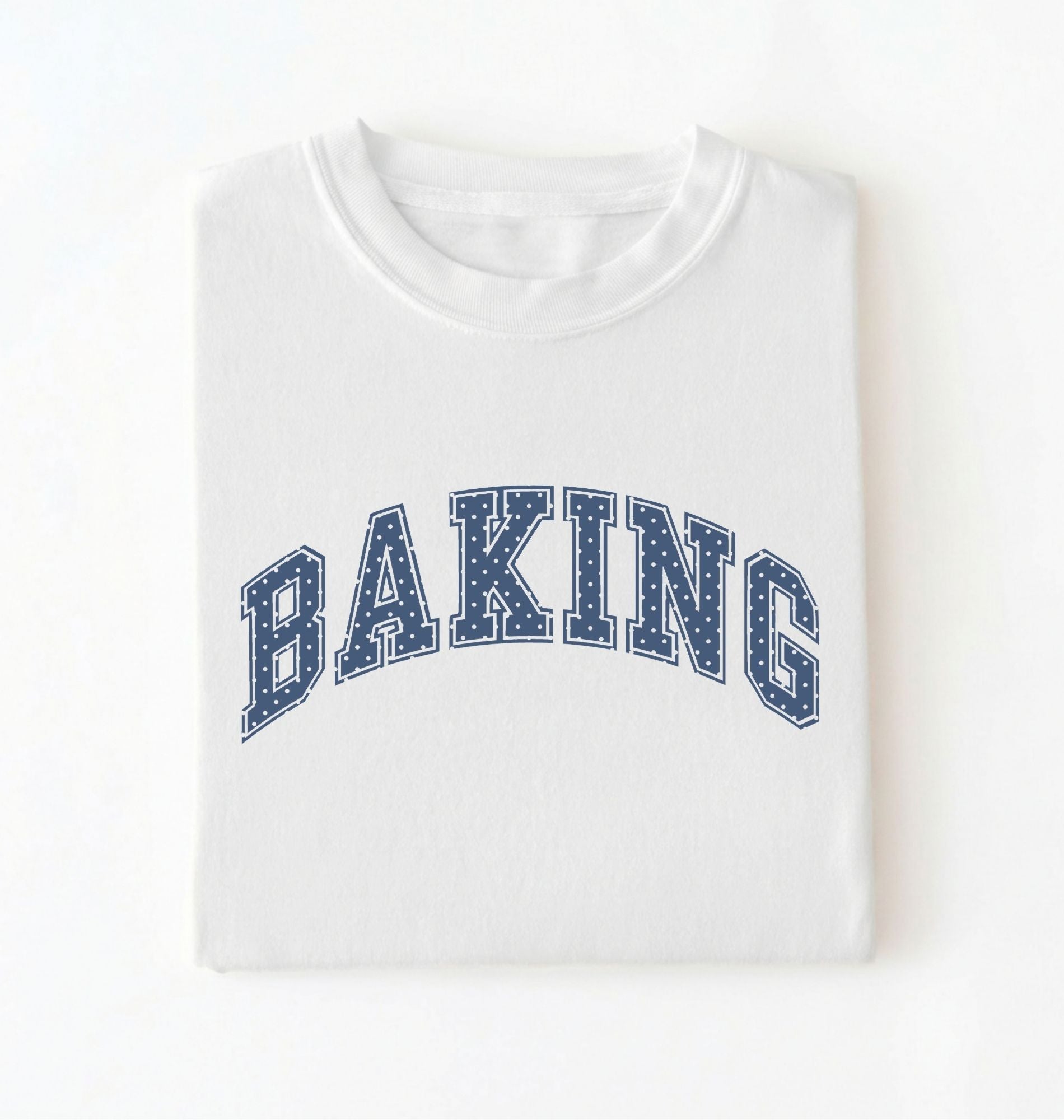 A folded white crewneck t-shirt with the word 'BAKING' printed in an arched navy blue varsity-style font with white dots, set against a plain white background.