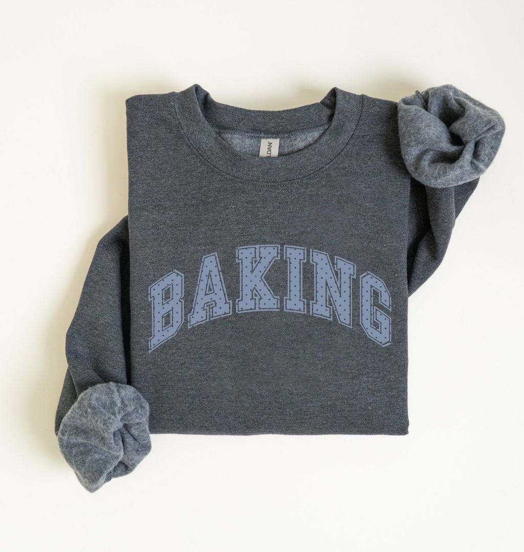 A folded dark heather gray sweatshirt with 'BAKING' printed across the chest in light blue varsity-style letters, shown on a plain off-white background.