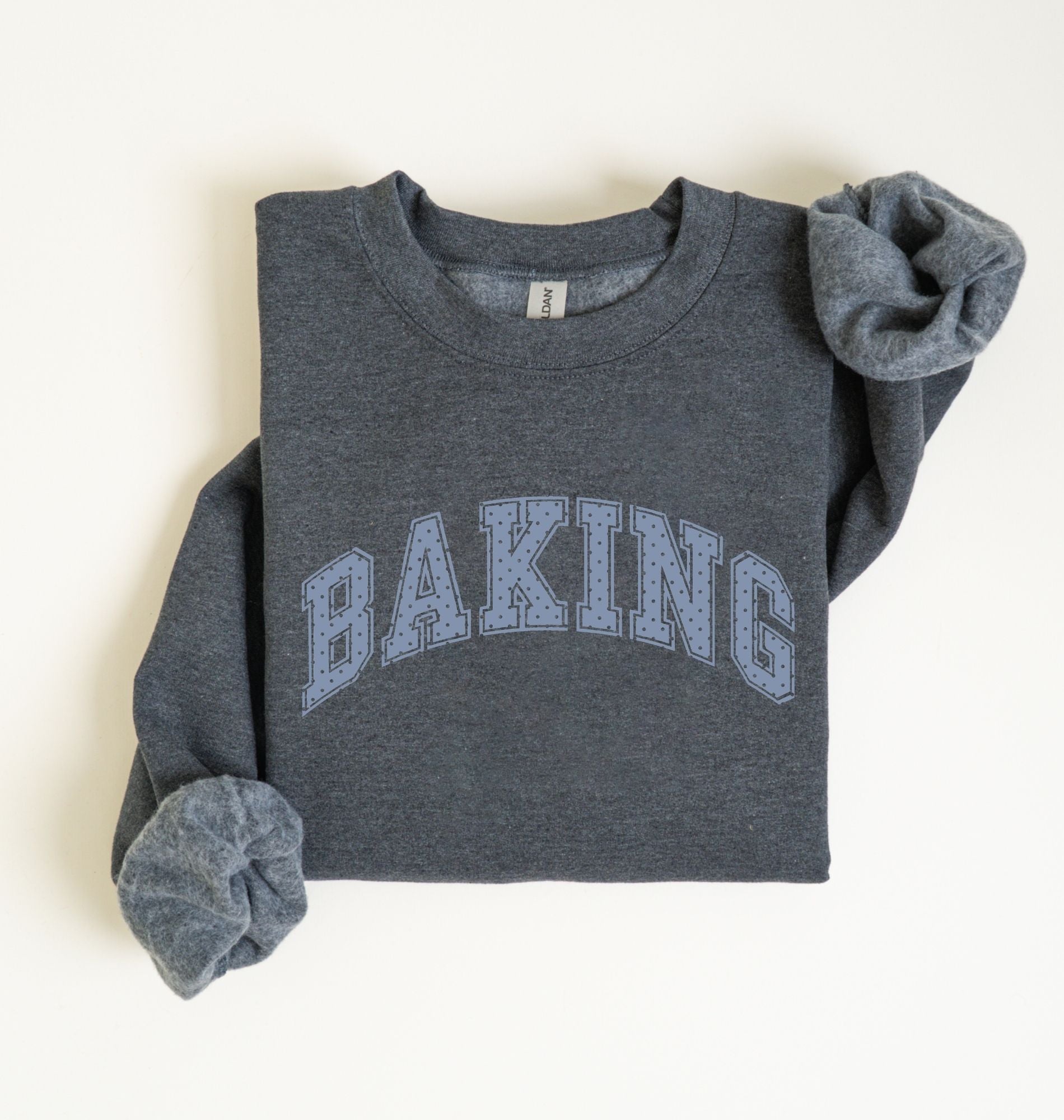 A folded dark heather gray sweatshirt with 'BAKING' printed across the chest in light blue varsity-style letters, shown on a plain off-white background.