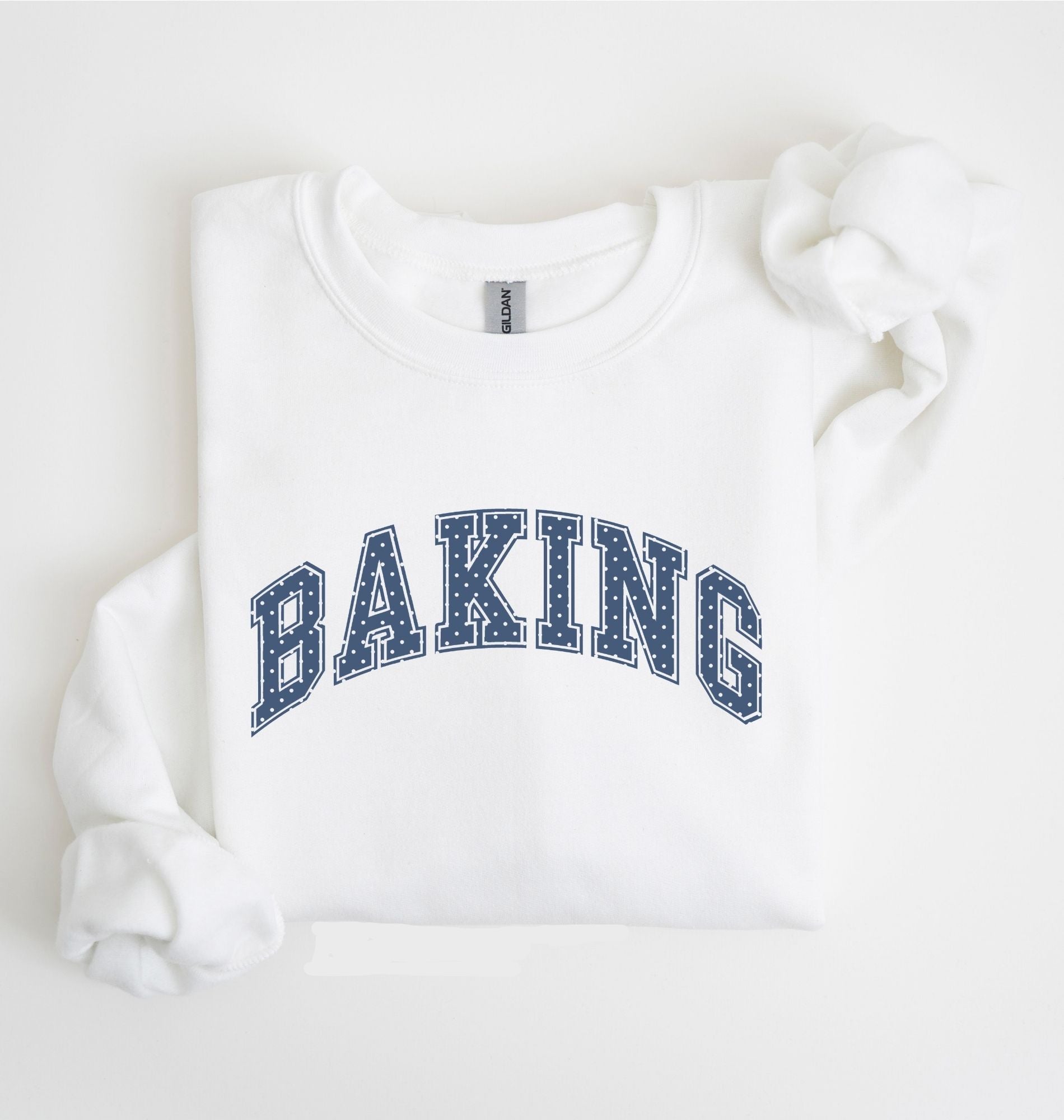 A white long-sleeve sweatshirt with 'BAKING' printed in navy blue varsity-style block letters across the chest, laid flat on a white background.