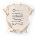 Flat ay of a Vintage baking tools shirt with whisk rolling pin and spatula illustrations on cream tee on a white background 