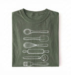 Flat ay of a Vintage baking tools shirt with whisk rolling pin and spatula illustrations on green tee on a white background 