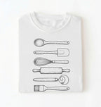 Flat ay of a Vintage baking tools shirt with whisk rolling pin and spatula illustrations on white tee on a white background 
