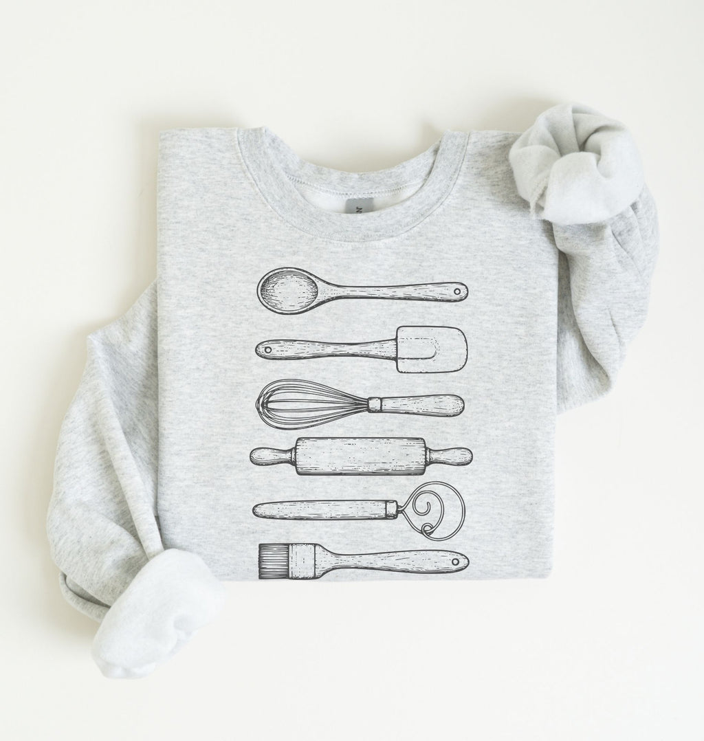 Flat lay of an ash Vintage baking tools sweatshirt featuring whisk rolling pin spatula and kitchen utensil illustrations on a white background 