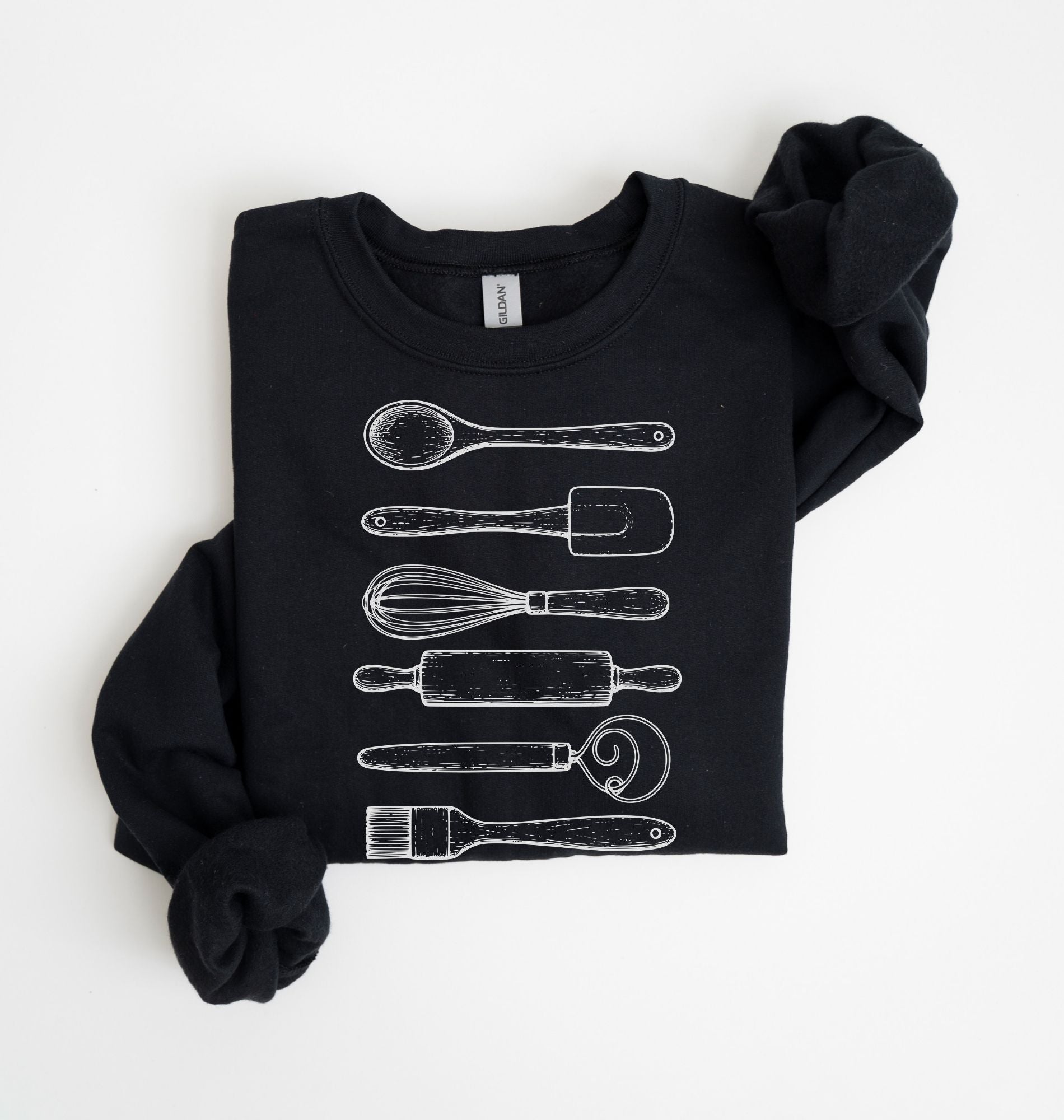 Flat lay of a black Vintage baking tools sweatshirt featuring whisk rolling pin spatula and kitchen utensil illustrations on a white background 