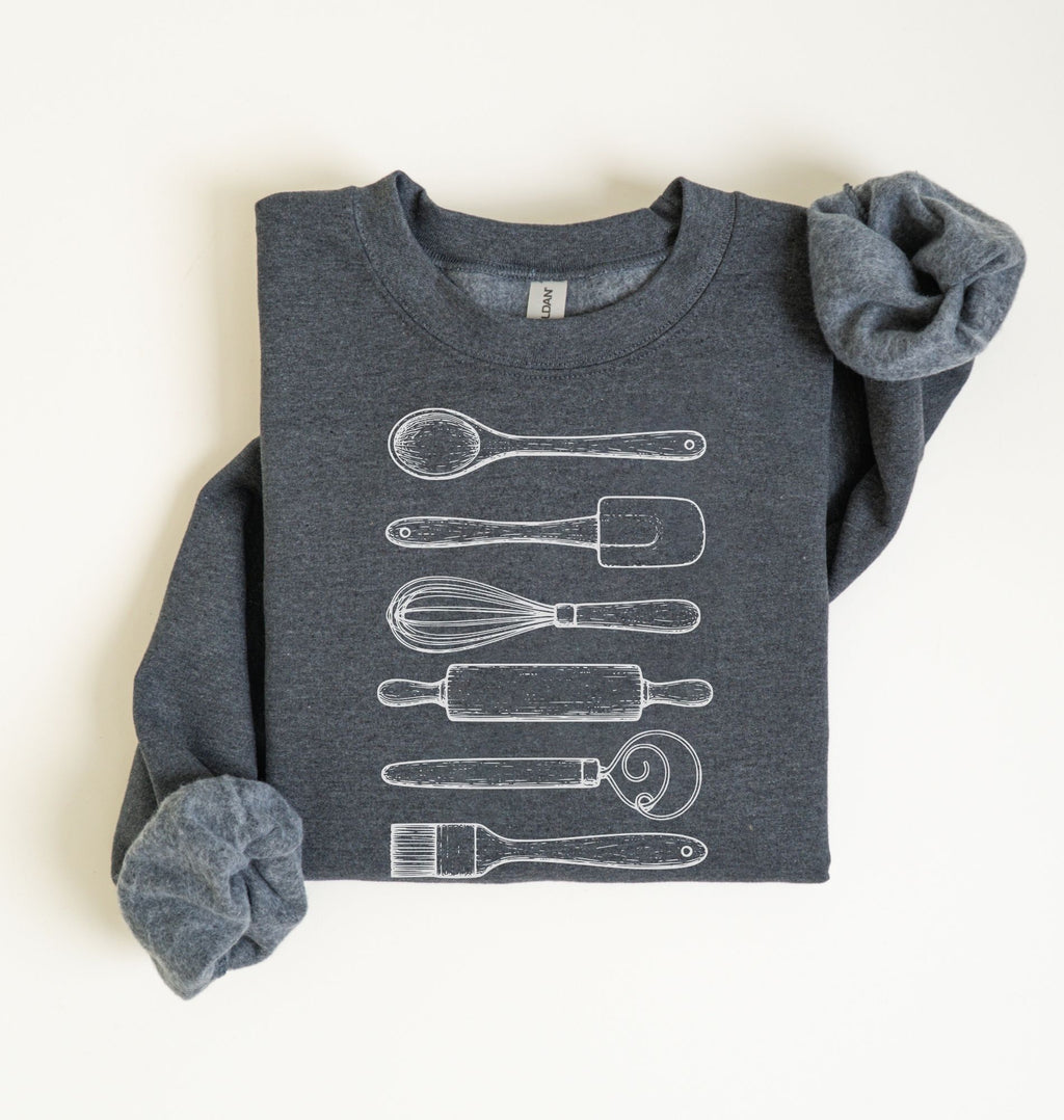 Flat lay of a dark heather Vintage baking tools sweatshirt featuring whisk rolling pin spatula and kitchen utensil illustrations on a white background 