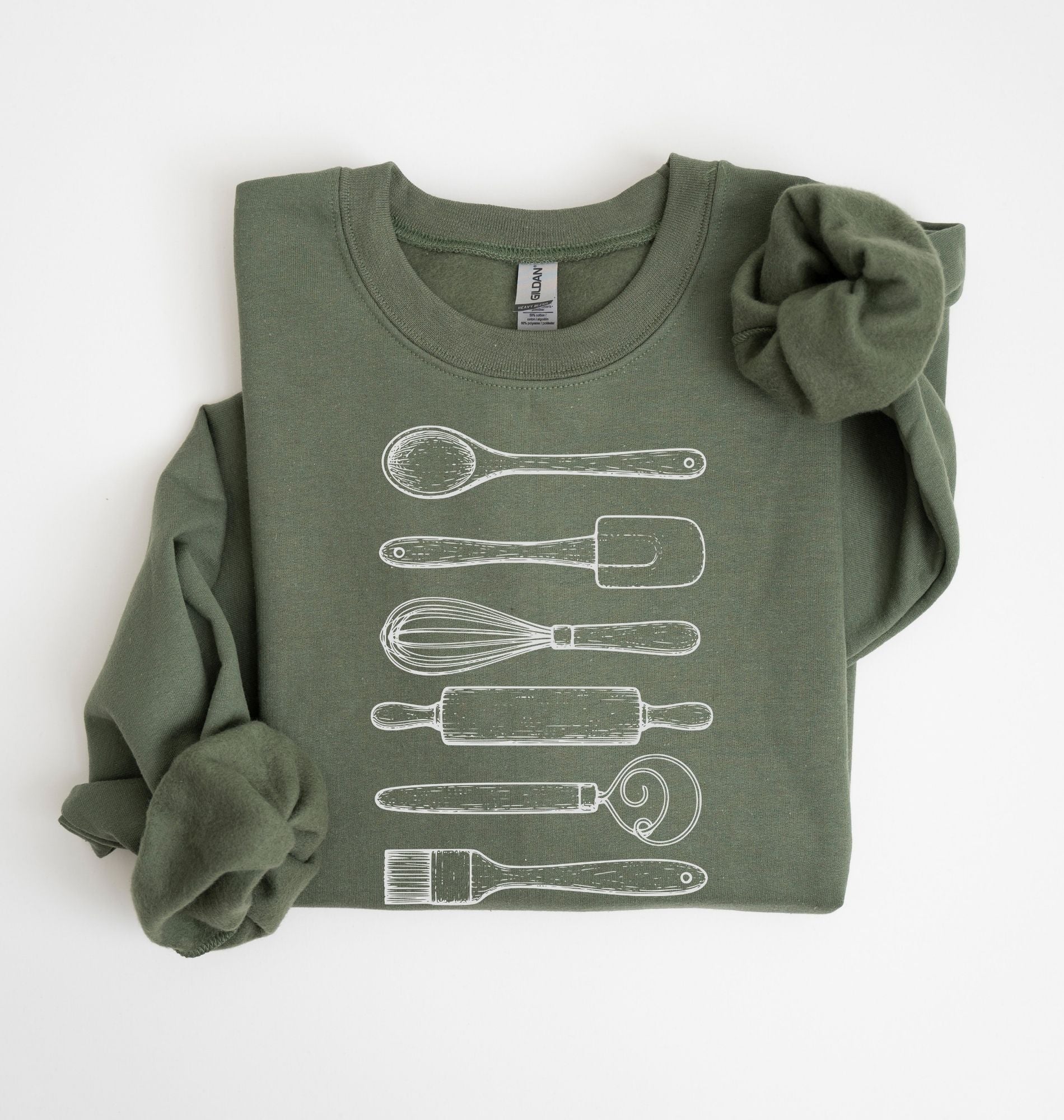 Flat lay of a military green Vintage baking tools sweatshirt featuring whisk rolling pin spatula and kitchen utensil illustrations on a white background 