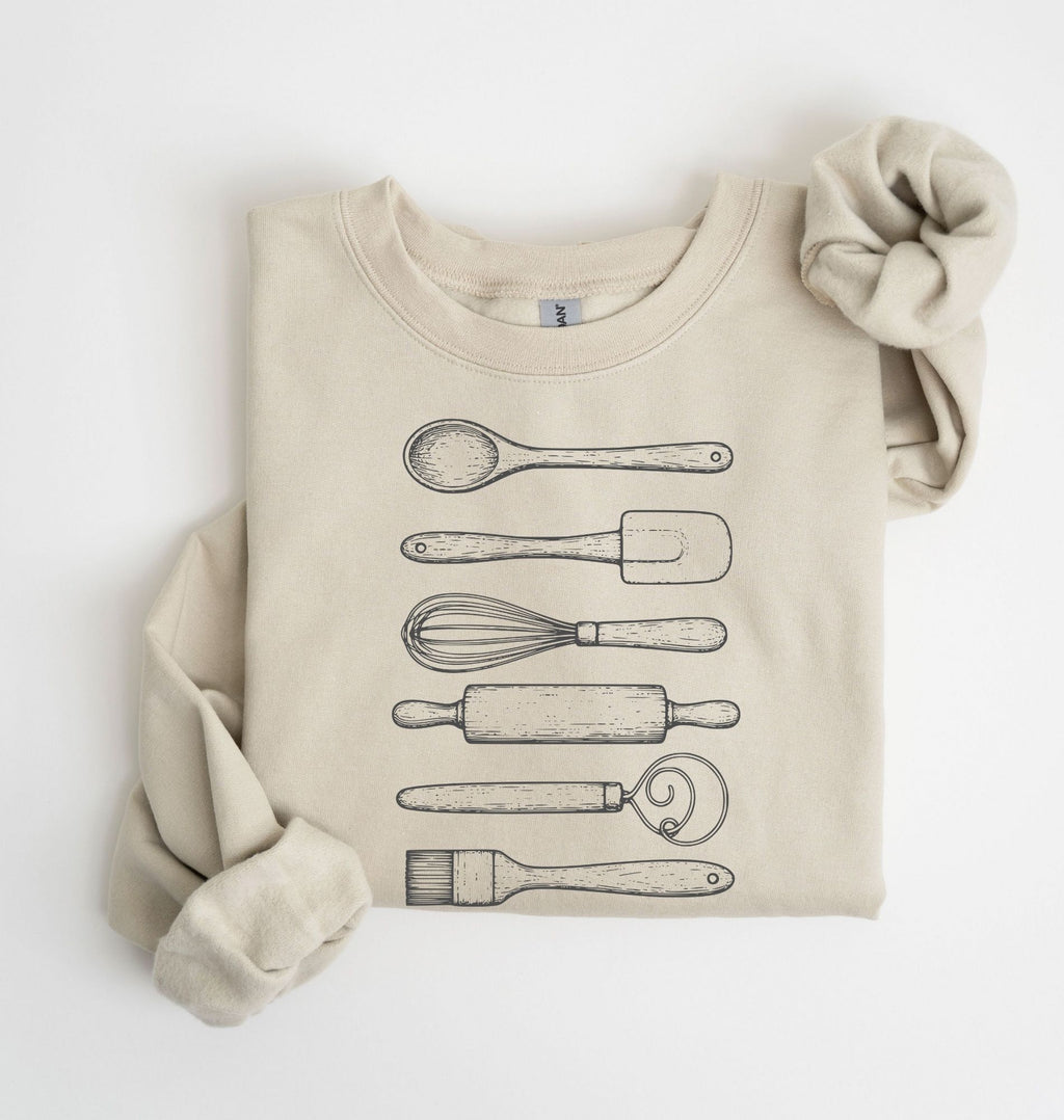 Flat lay of a sand Vintage baking tools sweatshirt featuring whisk rolling pin spatula and kitchen utensil illustrations on a white background 