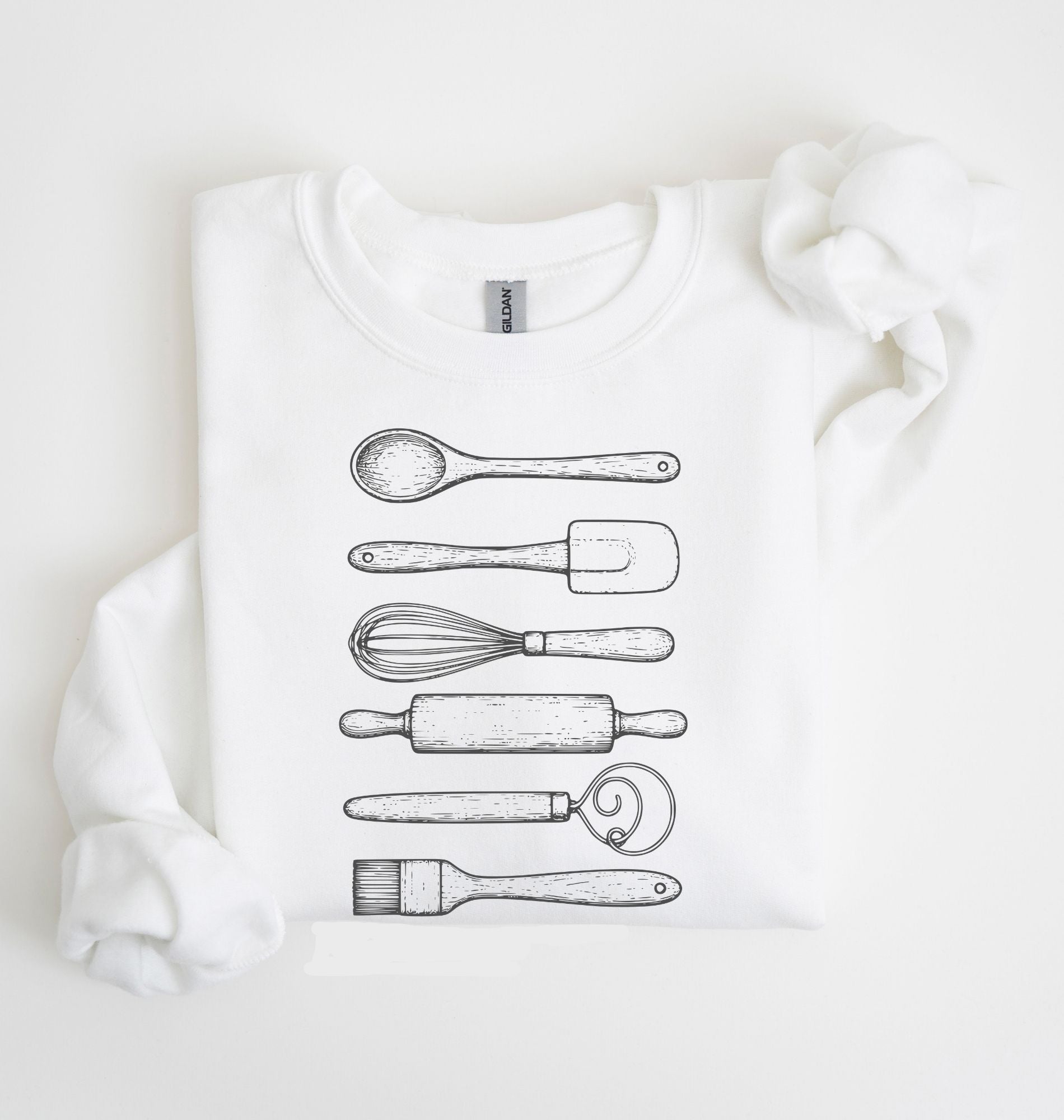 Flat lay of a white Vintage baking tools sweatshirt featuring whisk rolling pin spatula and kitchen utensil illustrations on a white background 