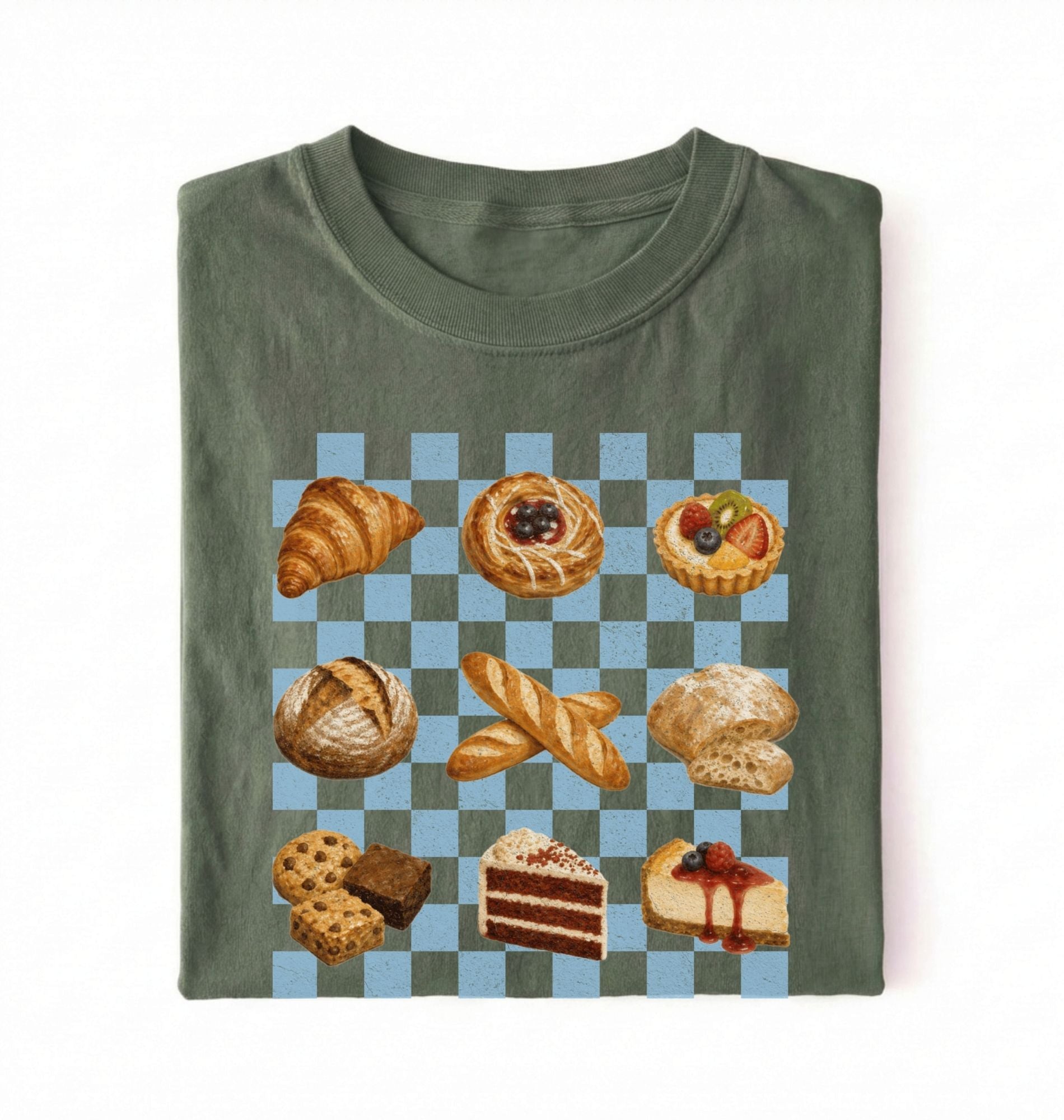 A folded olive green t-shirt with a graphic print of various pastries and cakes arranged on a light blue and gray checkered board, set against a plain white background.