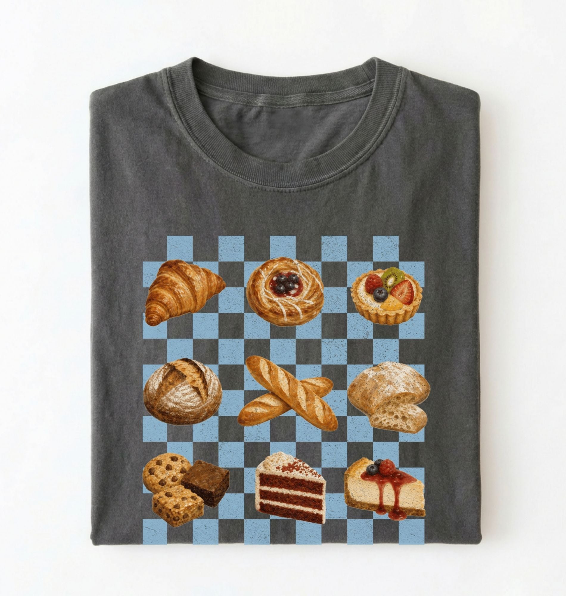 A folded dark gray t-shirt on a white background, featuring a graphic print of various pastries and cakes arranged on a blue and gray checkered board 