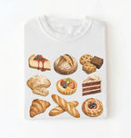 A white crewneck t-shirt featuring a graphic print of various illustrated pastries, breads, cakes, and cookies arranged in a grid, shown against a plain white background.