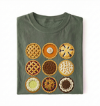 A folded sage green t-shirt featuring a graphic of nine embroidered-style pies in various flavors and patterns, displayed on a clean white background.