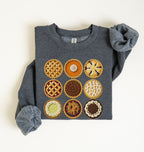 A folded dark heather gray sweatshirt with rolled sleeves, featuring a graphic of nine colorful pie designs on the front, laid flat on a light cream background.