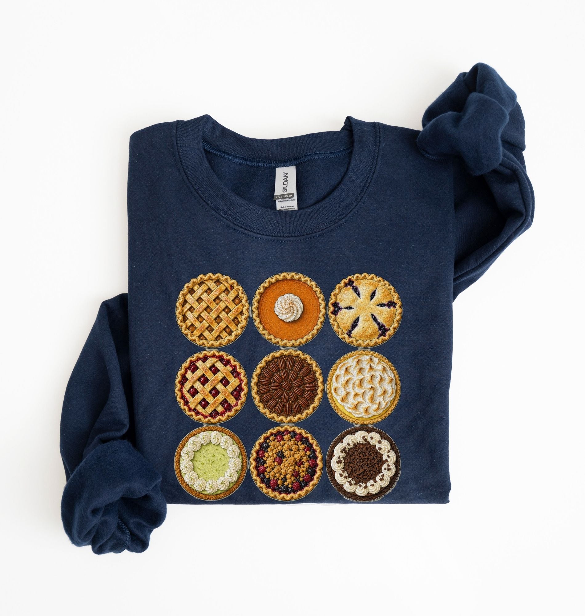A navy blue crewneck sweatshirt with a graphic of nine different mini pies arranged in a 3x3 grid on the front. The sweatshirt is shown folded with one sleeve rolled up, on a clean white background.
