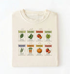 Flat lay of a cream vintage seed packet garden shirt with heirloom vegetable and herb illustrations gardener gift on a white background