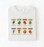 Flat lay of a white vintage seed packet garden shirt with heirloom vegetable and herb illustrations gardener gift on a white background