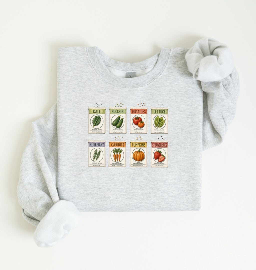 Flat lay of an ash vintage seed packet garden sweatshirt with heirloom vegetable and herb illustrations gardener gift on a white background 