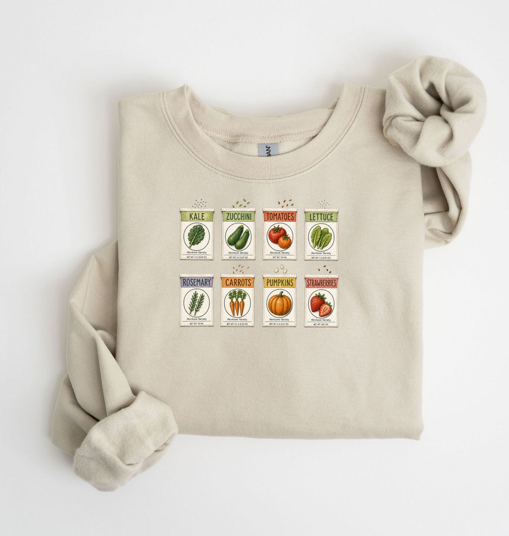 Flat lay of an sand vintage seed packet garden sweatshirt with heirloom vegetable and herb illustrations gardener gift on a white background 