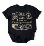 Flat lay of a black wait i see an antique store shirt funny vintage thrift aesthetic gift on a white background 