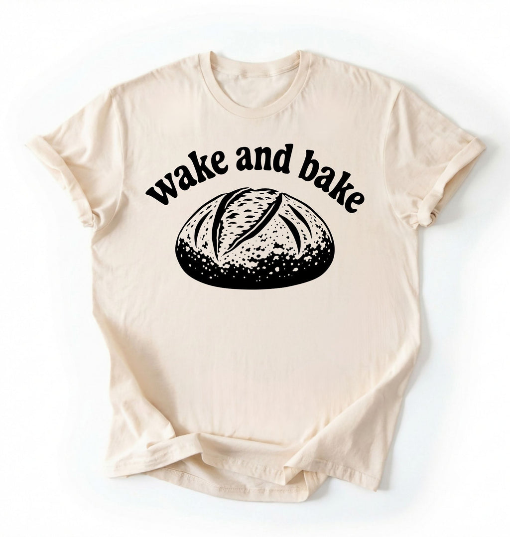 Flat lay of a Funny wake and bake bread shirt with rustic loaf illustration on cream tee on a white background