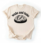 Flat lay of a Funny wake and bake bread shirt with rustic loaf illustration on cream tee on a white background