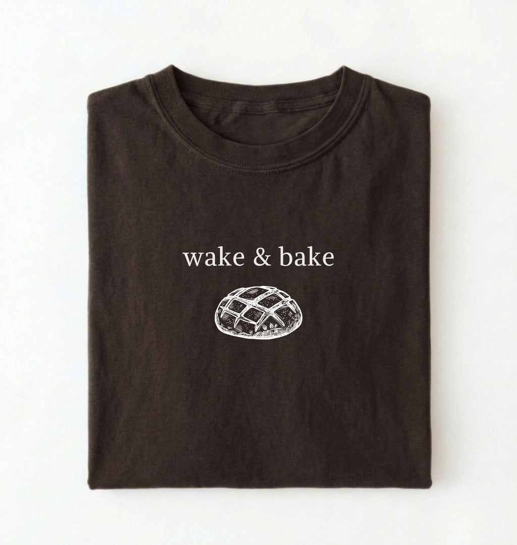 Flat lay of a dark chocolate Funny wake and bake bread shirt perfect for bakers bread lovers and home baking enthusiasts on a white background 