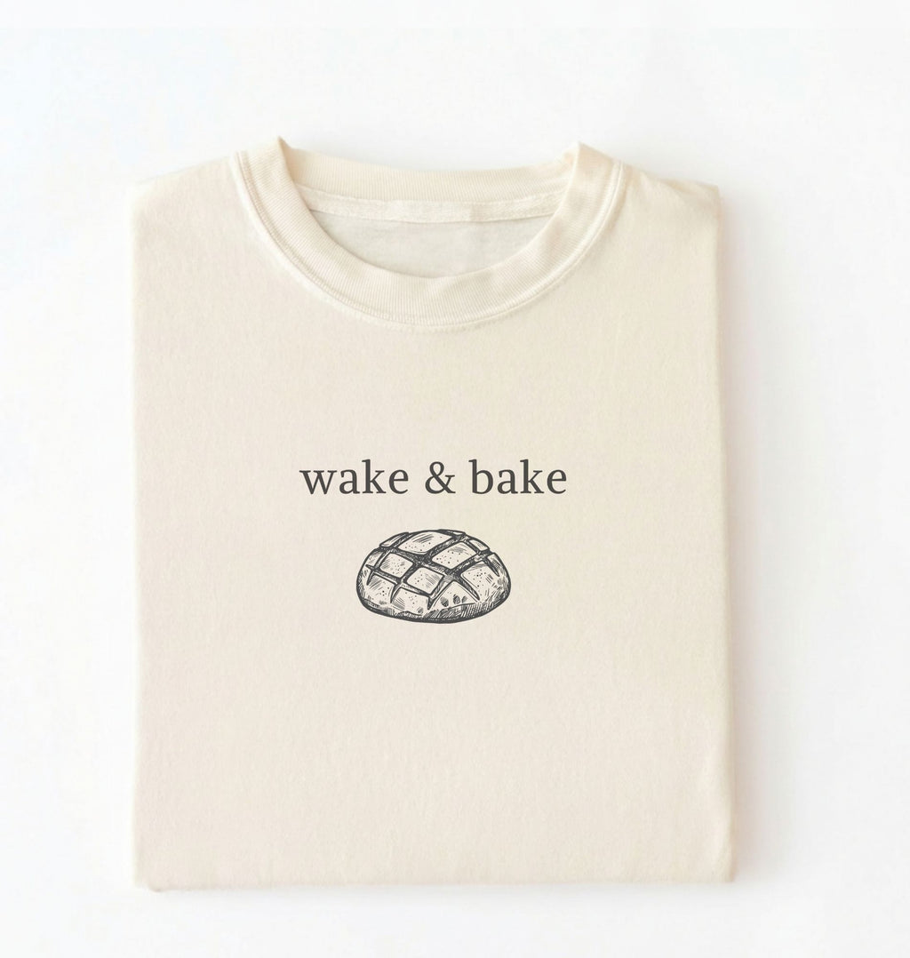 Flat lay of an ivory Funny wake and bake bread shirt perfect for bakers bread lovers and home baking enthusiasts on a white background