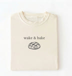 Flat lay of an ivory Funny wake and bake bread shirt perfect for bakers bread lovers and home baking enthusiasts on a white background