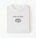 Flat lay of a white Funny wake and bake bread shirt perfect for bakers bread lovers and home baking enthusiasts on a white background