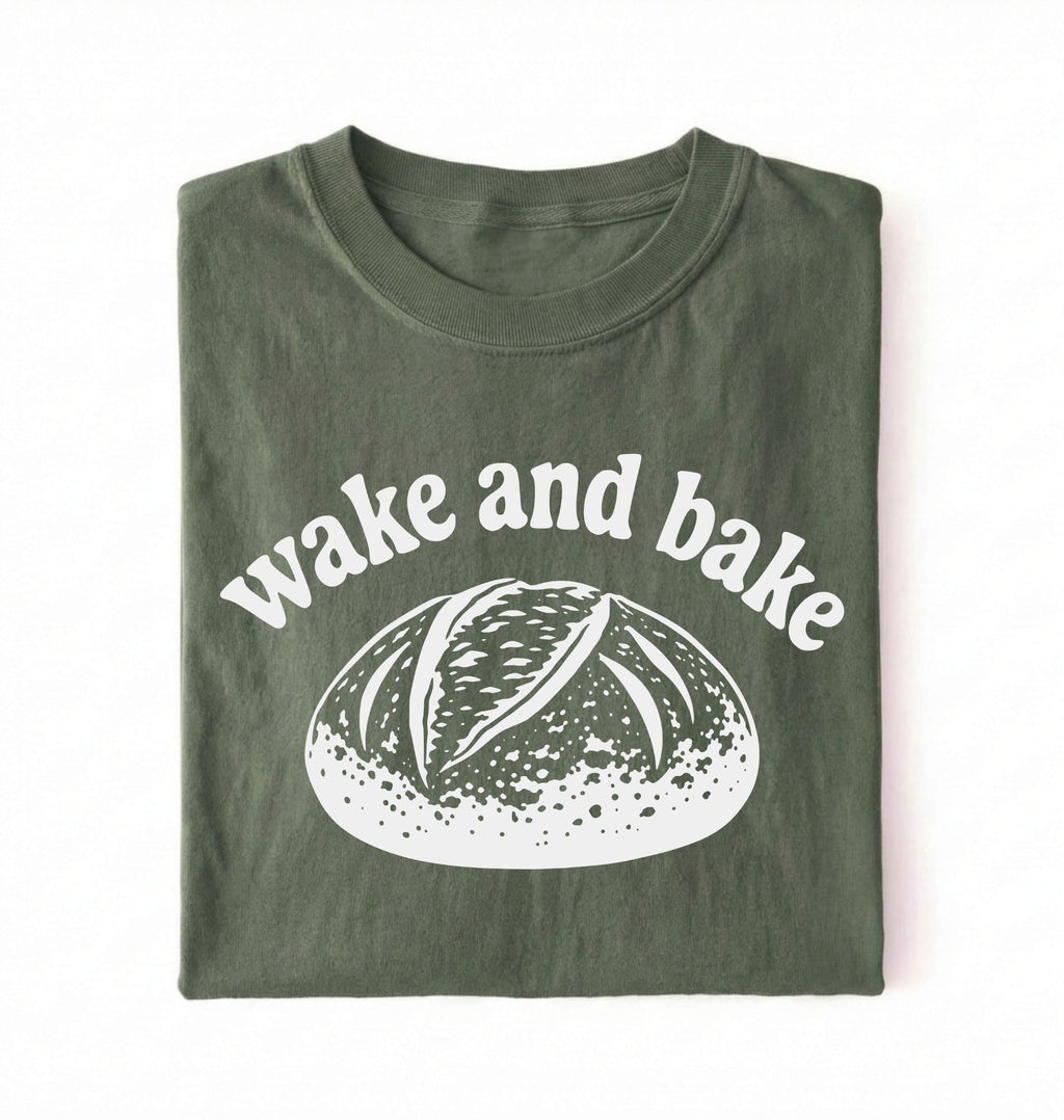Flat lay of a Funny wake and bake bread shirt with rustic loaf illustration on green tee on a white background