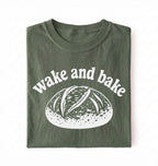 Flat lay of a Funny wake and bake bread shirt with rustic loaf illustration on green tee on a white background