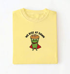 Flat lay of a Cornsilk Funny We Rise At Dawn frog baker shirt featuring bread loaf graphic for sourdough enthusiasts on a white background 