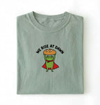 Flat lay of a bay Funny We Rise At Dawn frog baker shirt featuring bread loaf graphic for sourdough enthusiasts on a white background 