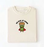 Flat lay of a ivory Funny We Rise At Dawn frog baker shirt featuring bread loaf graphic for sourdough enthusiasts on a white background 