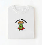 Flat lay of a white Funny We Rise At Dawn frog baker shirt featuring bread loaf graphic for sourdough enthusiasts on a white background 