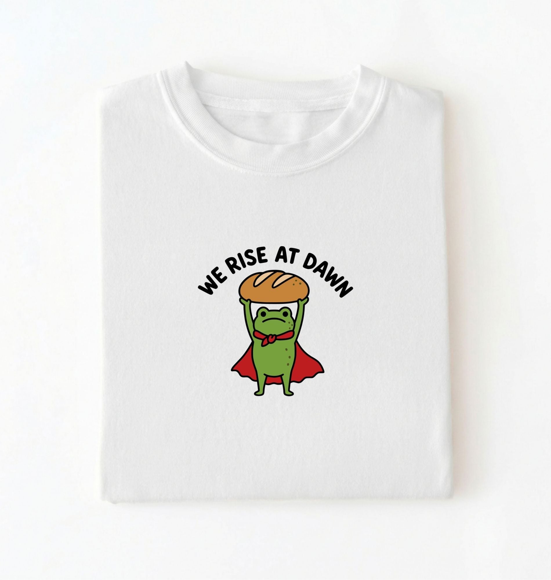 Flat lay of a white Funny We Rise At Dawn frog baker shirt featuring bread loaf graphic for sourdough enthusiasts on a white background 