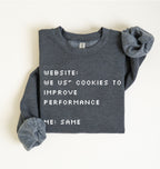 A folded dark heather gray sweatshirt with white pixel-style text reading 'WEBSITE: WE US* COOKIES TO IMPROVE PERFORMANCE' and 'ME: SAME', shown on a plain light background.
